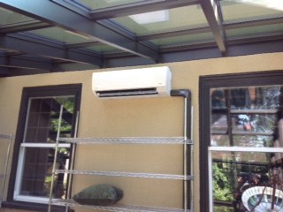 Wall‑mounted split air conditioner installed above windows on a covered patio or sunroom, providing cooling for a residential outdoor living space.