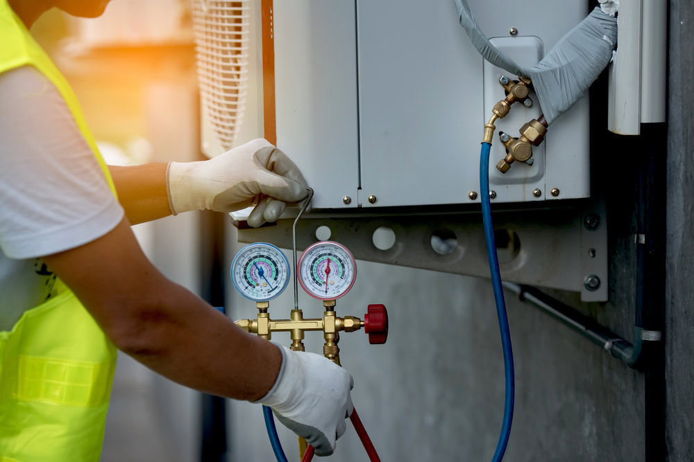 A technician wearing gloves checks the pressure on HVAC gauges while servicing an outdoor air conditioning unit, providing emergency HVAC service Long Island and Queens, NY residents trust.