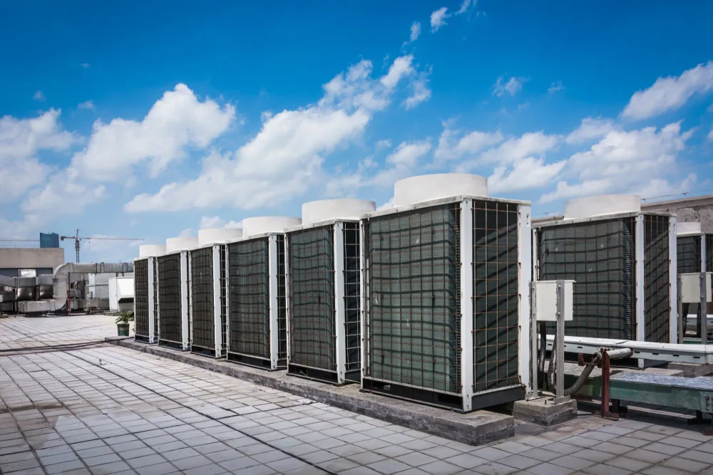 Rows of large HVAC units on a tiled rooftop under a blue sky with scattered clouds, showcasing part of an urban building’s air conditioning system—ready for emergency HVAC service in Long Island, NY or Queens.