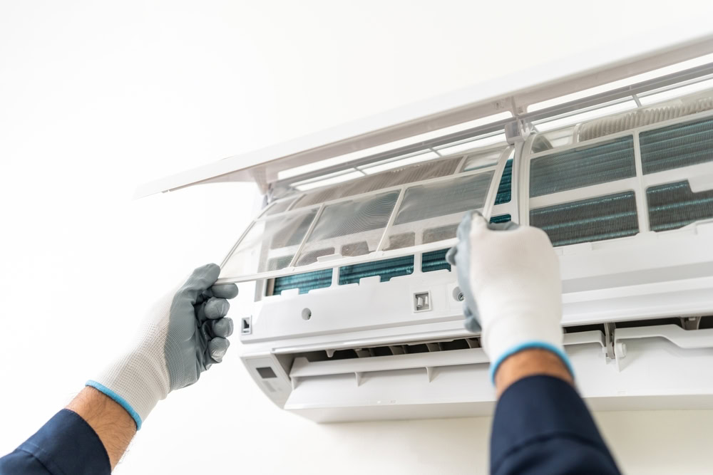 A person wearing gloves lifts the filter cover of a wall-mounted air conditioner in Queens, NY, preparing for cleaning or maintenance—an essential step often handled by emergency HVAC service Long Island professionals.